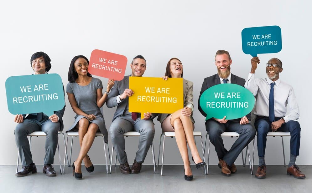 The Ultimate Guide to Diversity Hiring 7 A Diverse Group of People Holding Signs to Show They are Recruiting.