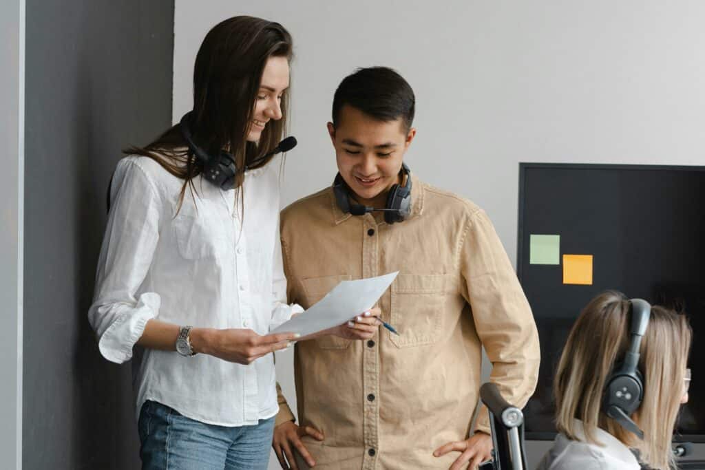 Optimizing Contact Center Recruitment: Leveraging Virtual Job Tryouts for Volume Hiring 5 Man and Woman smiling at a Piece of Paper in an Office